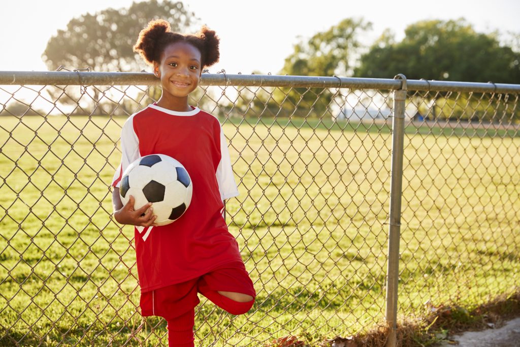 Girl holding soccer ball by fence
