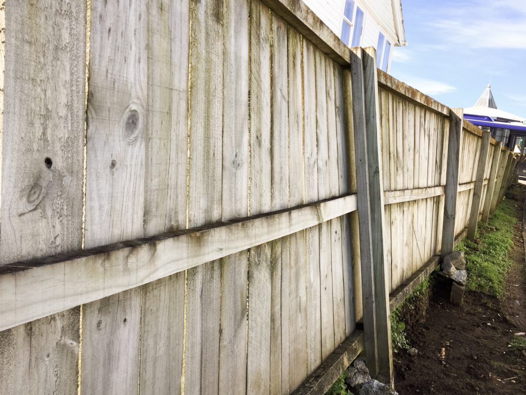 crooked wooden fence leaning and being dug out during repairs